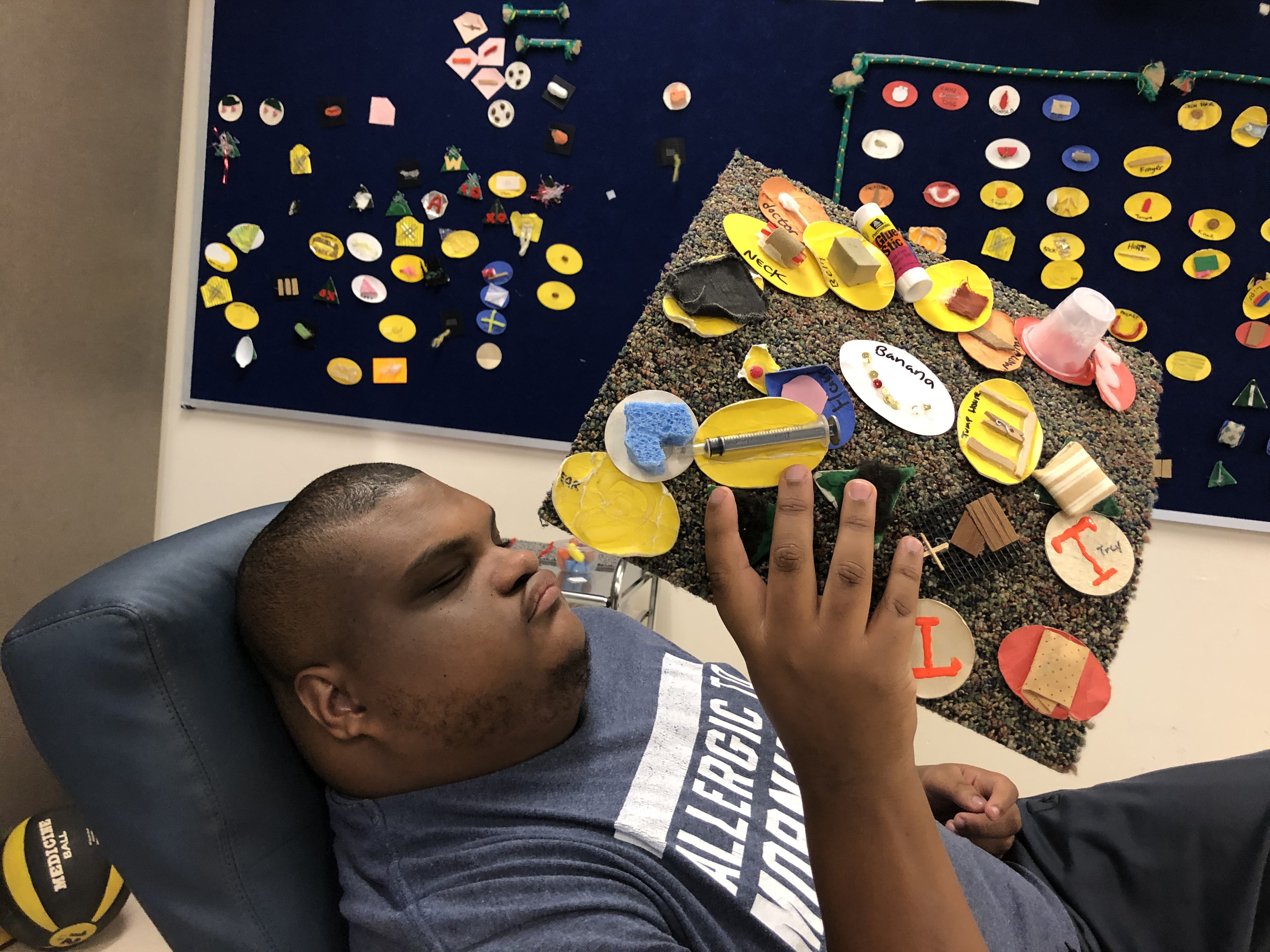 A young man holds up tactile symbol board while seated.