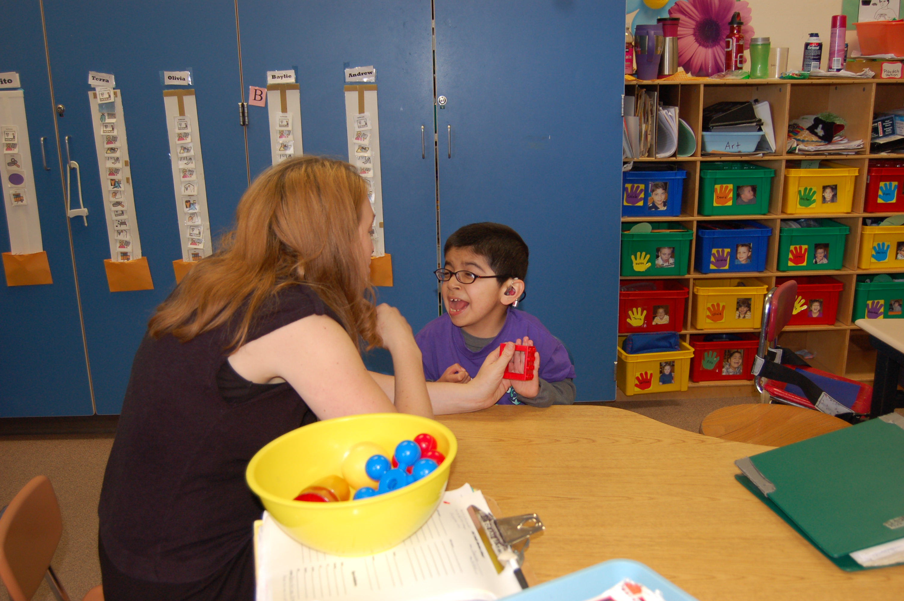 An aide and young boy are sitting at a table playing with a plastic toy.