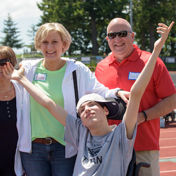 Adolescent boy who is deaf-blind at track meet. He's sitting in a wheelchair. His parents are standing behind him.