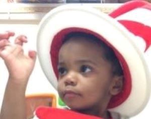 Young boy who is deaf-blind wearing a large white and red striped hat.