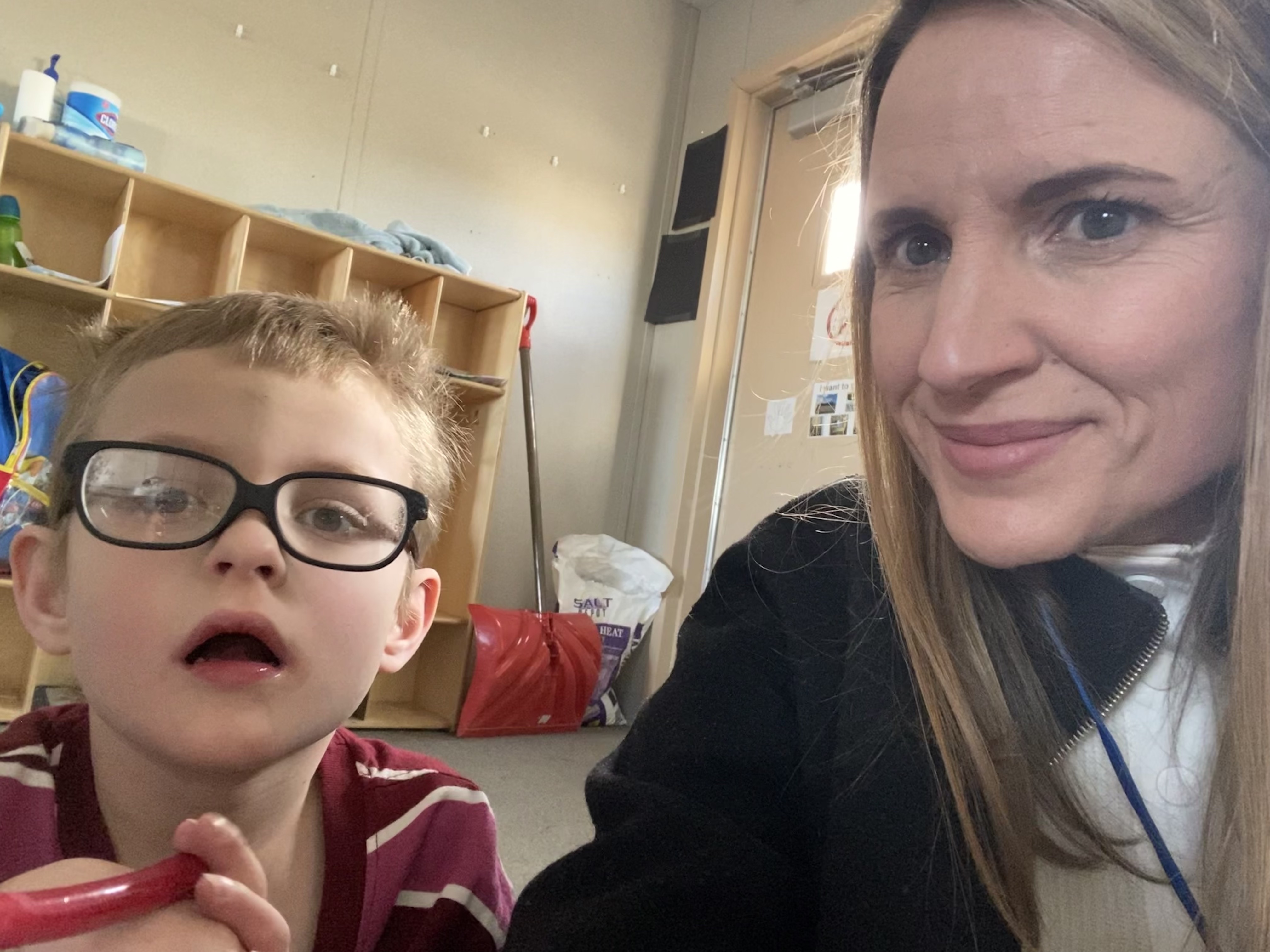 A young boy who is deafblind sits beside an adult female in a classroom setting.