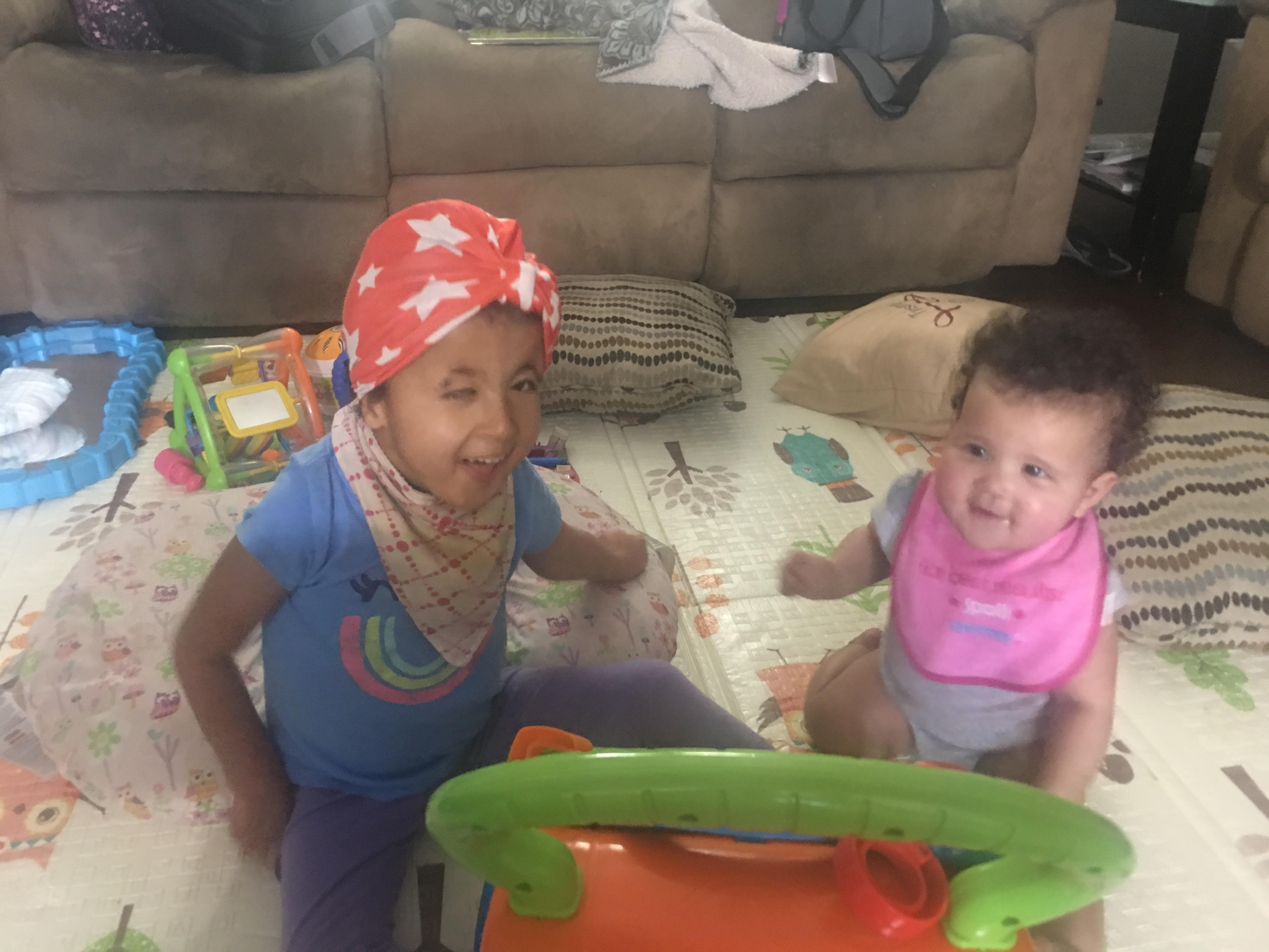 A young girl and infant playing on the floor of their living room.